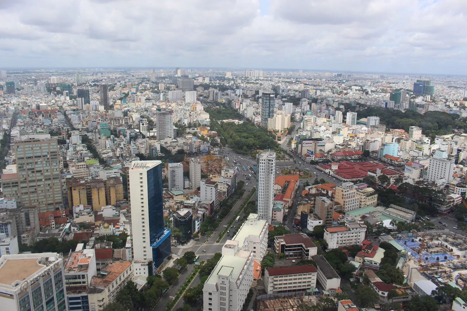 Aerial view of Ho Chi Minh City's dense skyline with high-rises stretching toward the horizon under a cloudy sky.