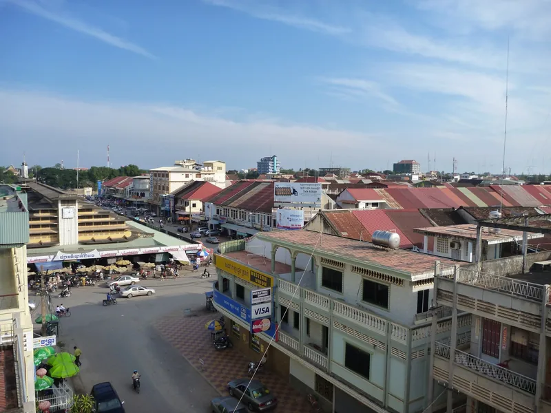Rooftop view over Battambang's market square and colorful shophouses under a wide sky.