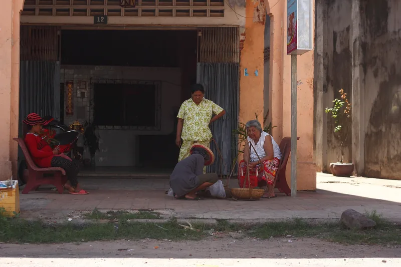 Locals gather and trade goods on a shaded street corner in Kampot, Cambodia.