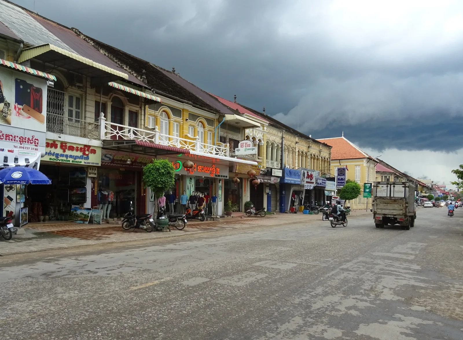 Colonial-era shophouses line a street in Battambang under a dramatic storm sky.