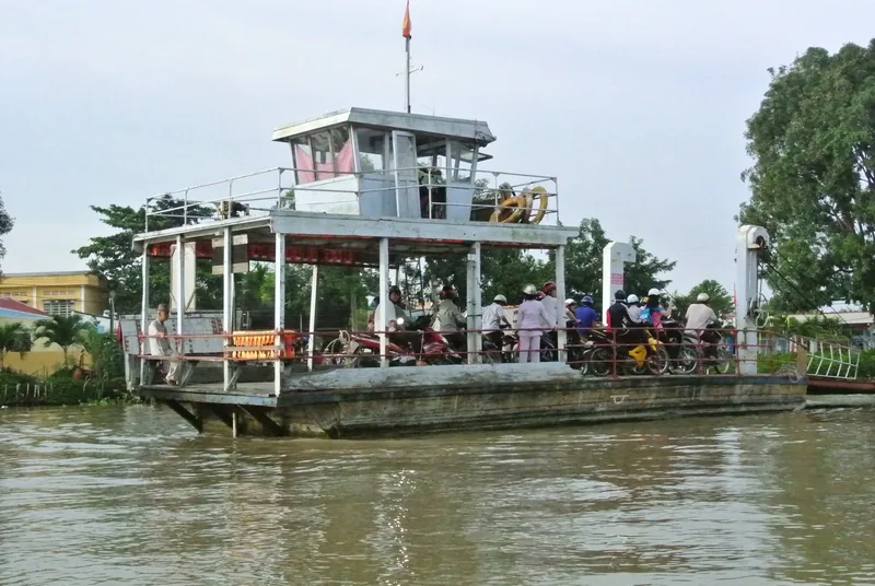 A car ferry crowded with motorbikes crosses a muddy river in the Mekong Delta
