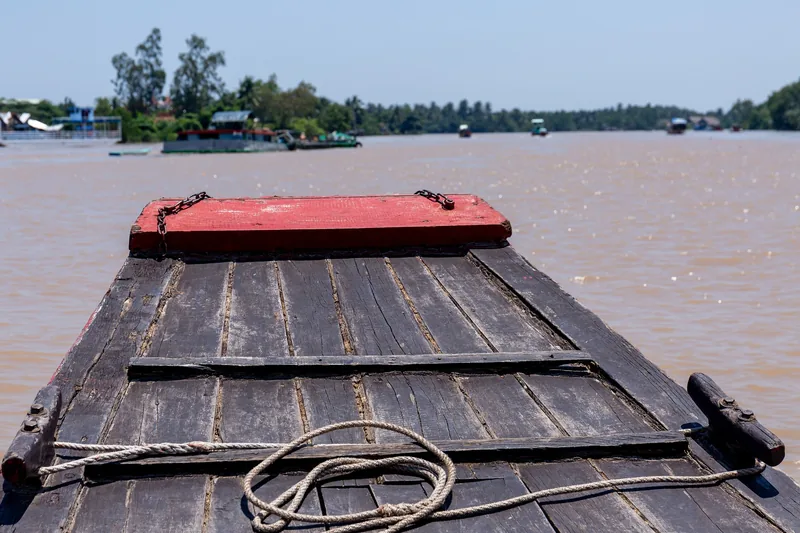 View from the bow of a wooden boat crossing the muddy waters of the Mekong Delta near Ben Tre.