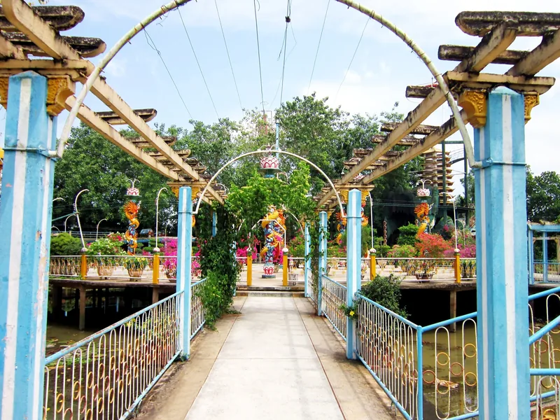 A decorated footbridge with dragon motifs and blue railings leads through a garden in the Mekong Delta.