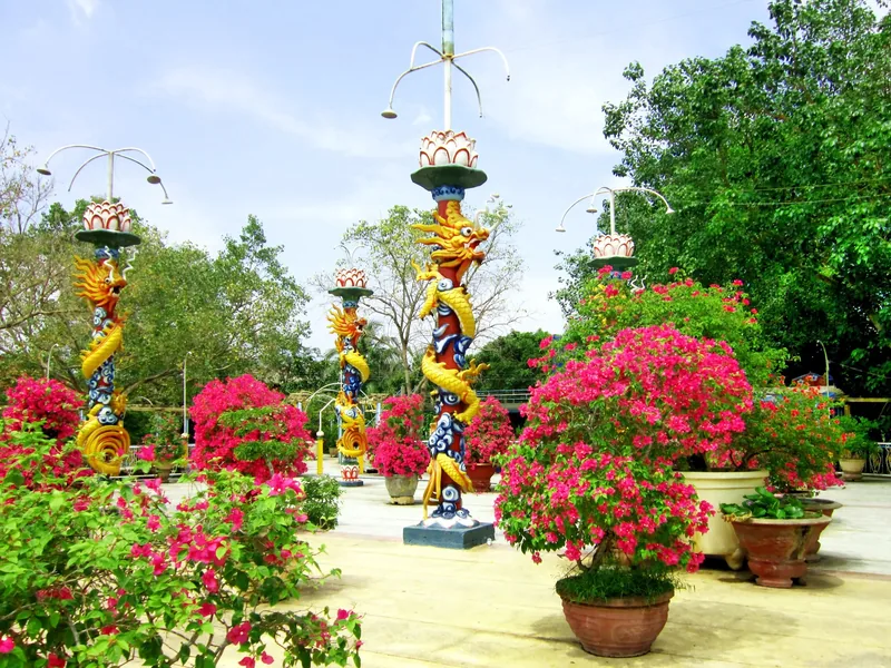Ornate dragon-carved pillars stand amid blooming bougainvillea in a garden in the Mekong Delta.