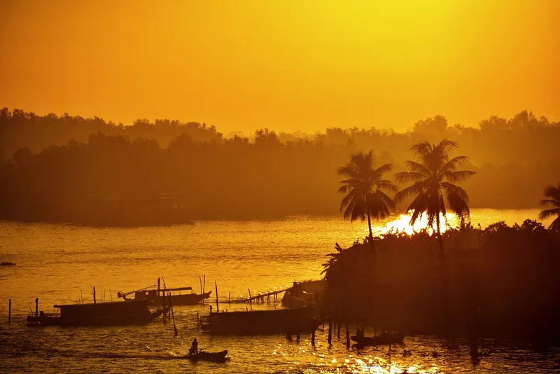 Golden sunset over the Can Tho River with silhouetted palm trees and small boats near Ninh Kieu, Can Tho.
