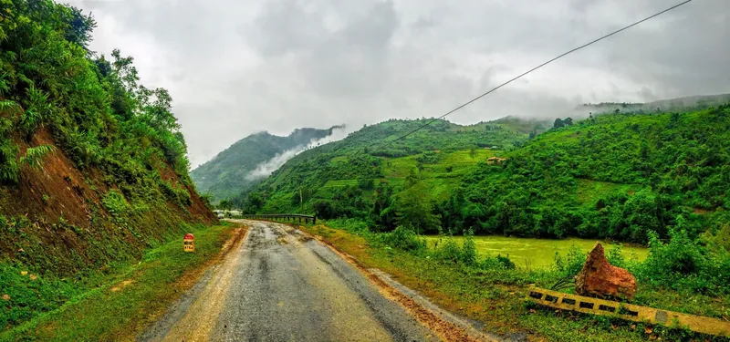 A misty mountain road winds through green hillsides in Cao Bang, Vietnam.