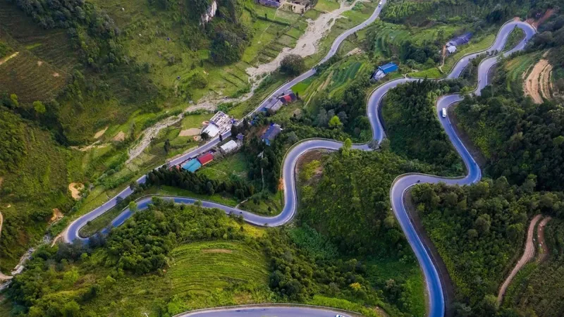 An aerial view captures a serpentine mountain road winding through green hills near Cao Bang.