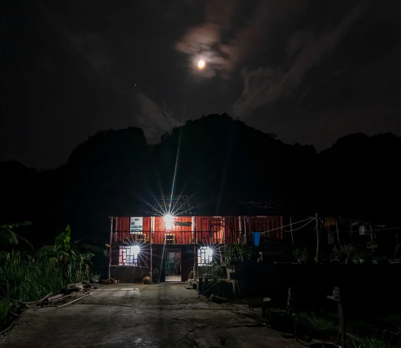 A stilt house glows under a bright moon against dark limestone hills in Cao Bang.