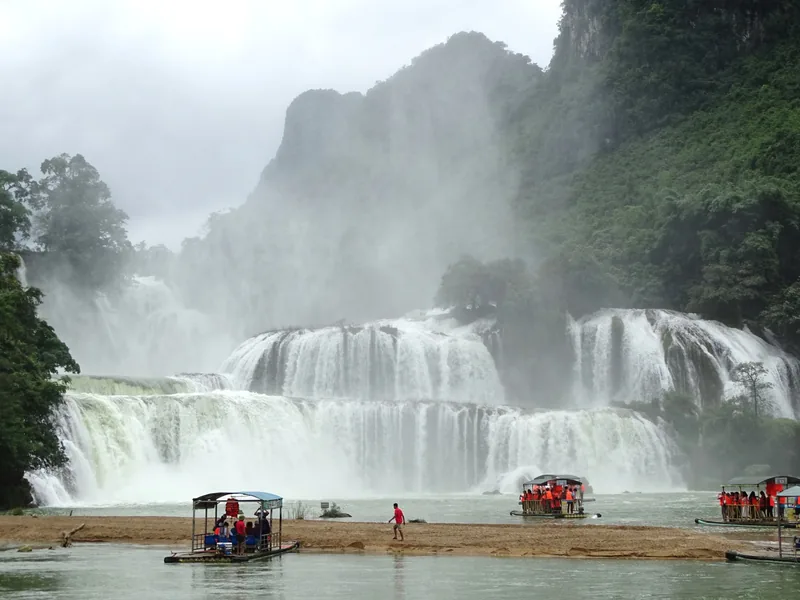 Rafts carry visitors across the river beneath the wide cascades of Ban Gioc Waterfall in Cao Bang.