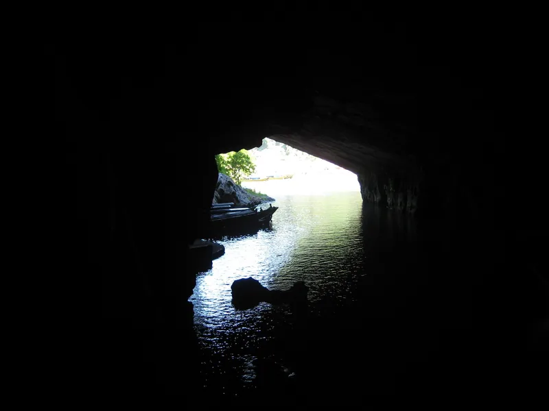 A boat floats on calm water at the mouth of a dark limestone cave in Phong Nha–Ke Bang National Park.