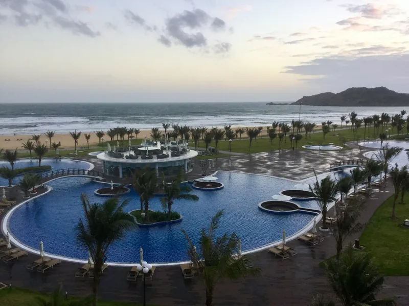 Curving resort swimming pools with palm trees line the beach at sunset in Quy Nhon.