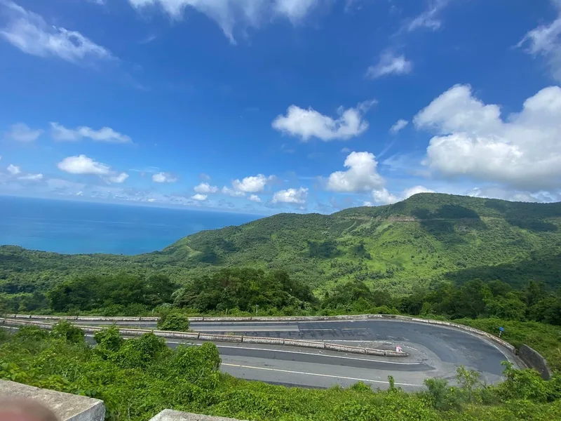 A winding switchback road curves along green mountains above the coastline on Hai Van Pass, Vietnam.