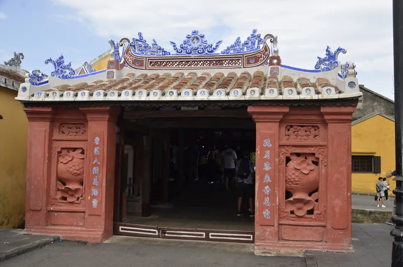 The ornate roof and red pillars of the Japanese Covered Bridge entrance in Hoi An's old town.