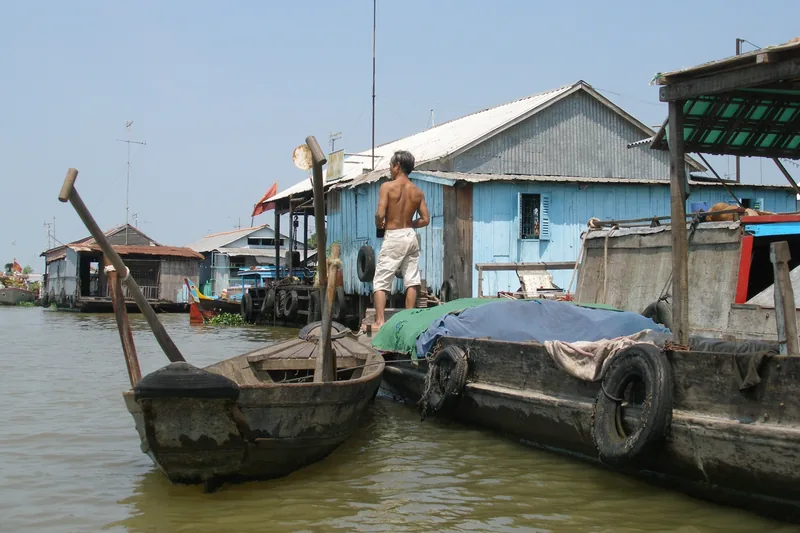 A man stands on a wooden boat beside floating houses on the river in Chau Doc, Vietnam.