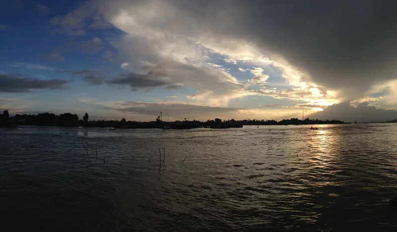 Dramatic clouds and sunset light over the wide river at Chau Doc, with boats silhouetted along the shore.