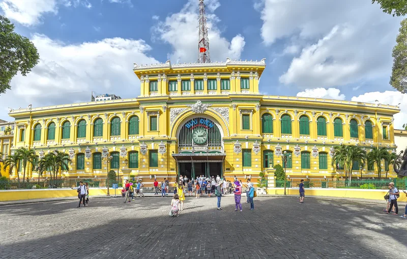 Yellow French colonial facade of Saigon Central Post Office with visitors gathered on the plaza below.