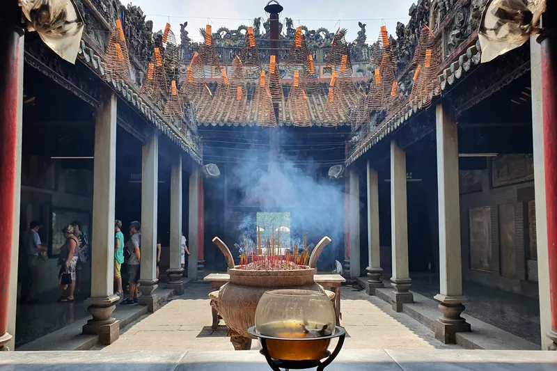 Spiral incense coils hang above a smoking bronze urn in a courtyard temple in Saigon.