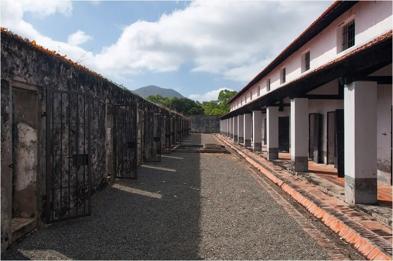 Rows of old prison cells with iron gates line a gravel courtyard at a historic site in Con Dao.