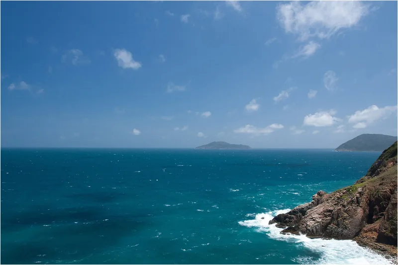 Turquoise sea meets rocky cliffs under a blue sky at Mui Ta Be, Con Dao islands.