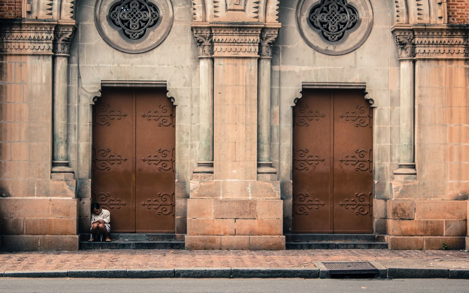 A person sits reading on the steps of an ornate stone church door in Ho Chi Minh City.