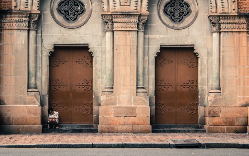 A person sits reading on the steps of an ornate stone church door in Ho Chi Minh City.