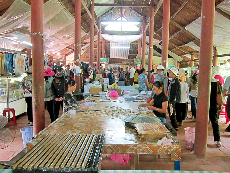 Workers roll coconut candy at a workshop table under a thatched roof in the Mekong Delta.