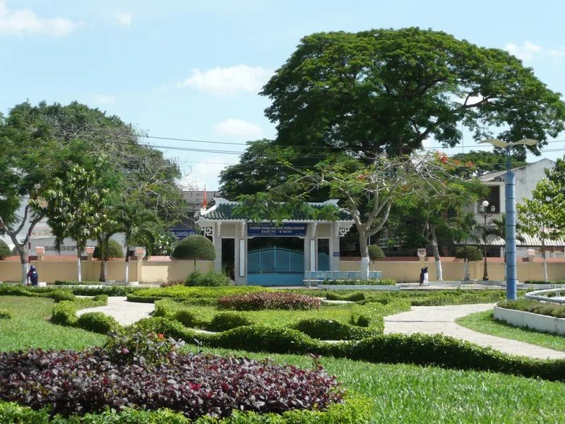 A landscaped park with manicured hedges and shady trees leads to a school gate in Ben Tre, Mekong Delta.