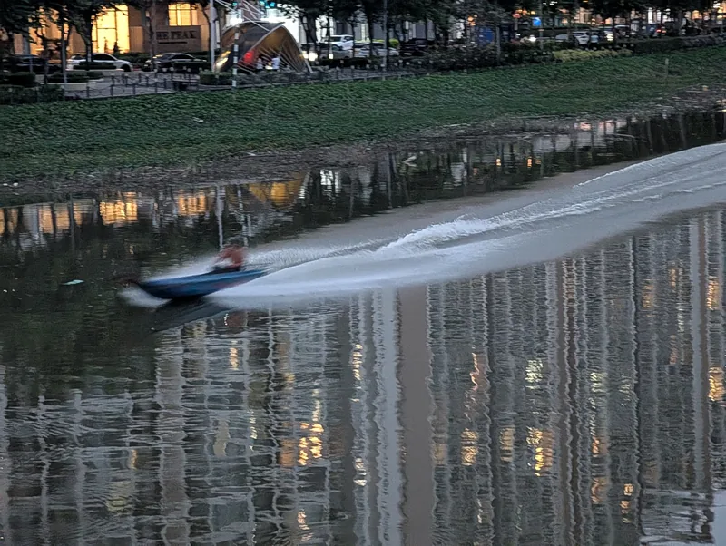 A speedboat leaves a trail of white wake on a canal at dusk in Ho Chi Minh City's Phu My Hung area.