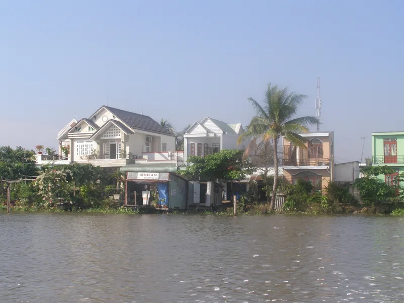 Riverside houses with a coconut palm line the muddy waterfront in the Cu Chi Tay Ninh area of Vietnam.