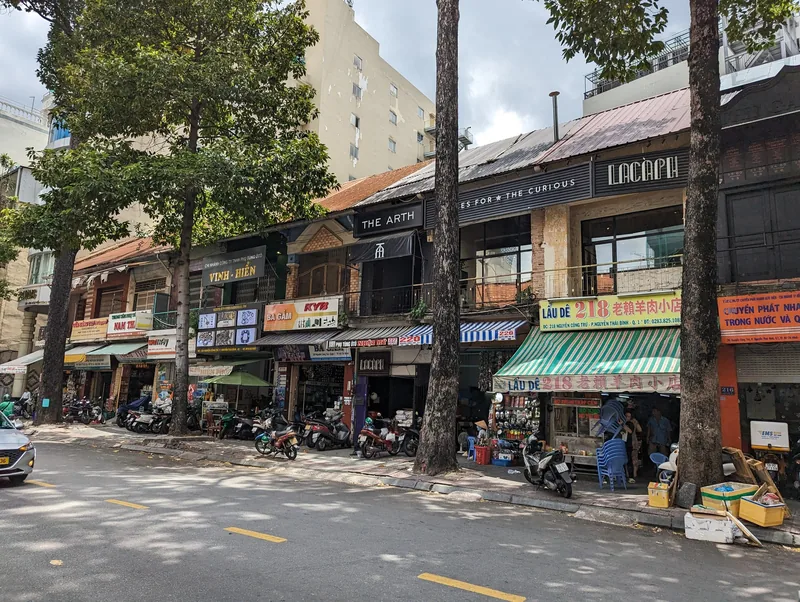 A tree-lined street in District 1, Ho Chi Minh City, lined with shophouses, cafes, and parked motorbikes.
