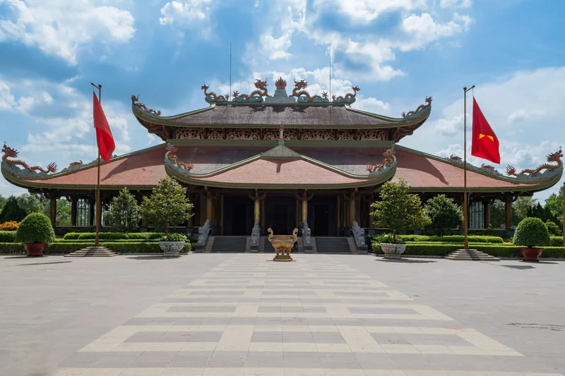 Ben Duoc Temple's ornate pagoda-style facade with Vietnamese flags stands before a wide stone courtyard in Cu Chi.