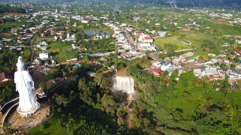Aerial view of Elephant Waterfall near Da Lat with a white statue and a town spreading across green hills.