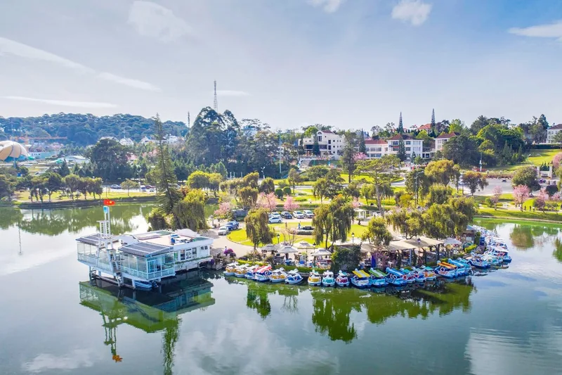 Colorful paddle boats dock along Xuan Huong Lake with green parks and villas in Da Lat's town center.
