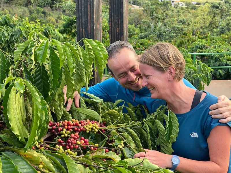 A smiling couple lean in to admire ripe coffee cherries on a plant during a coffee farm visit near Da Lat.