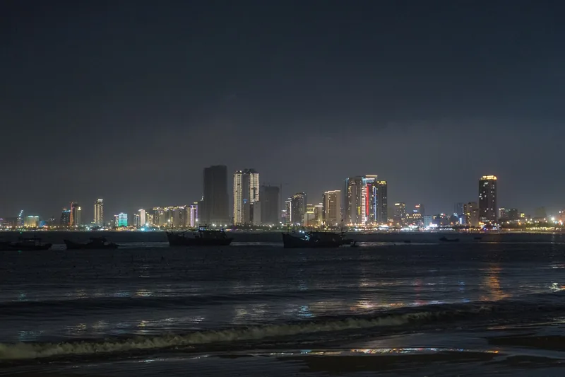 Fishing boats float offshore as the illuminated skyline of Da Nang glows at night.