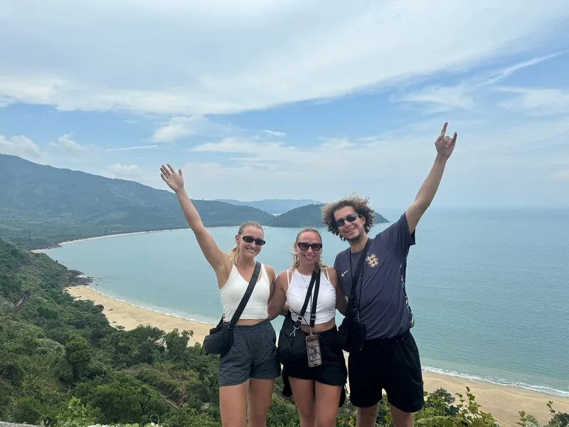 Travelers pose with raised arms above a curving beach along the coastal road between Hue and Hoi An, Vietnam.