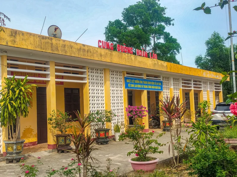 A yellow-painted single-story building with a red signboard reading Cung Duong Hoan Lao, potted plants along its front.