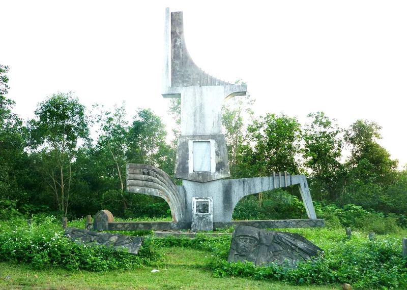 A weathered concrete war memorial monument stands amid greenery at the former Camp Carroll site in Quang Tri, Vietnam.