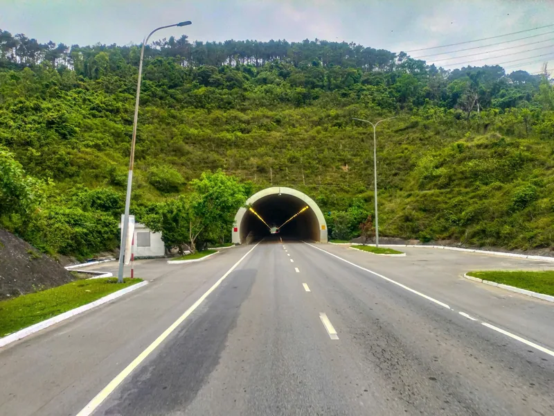 A road tunnel entrance cuts through a green, tree-covered hill on a highway in Quang Tri province.