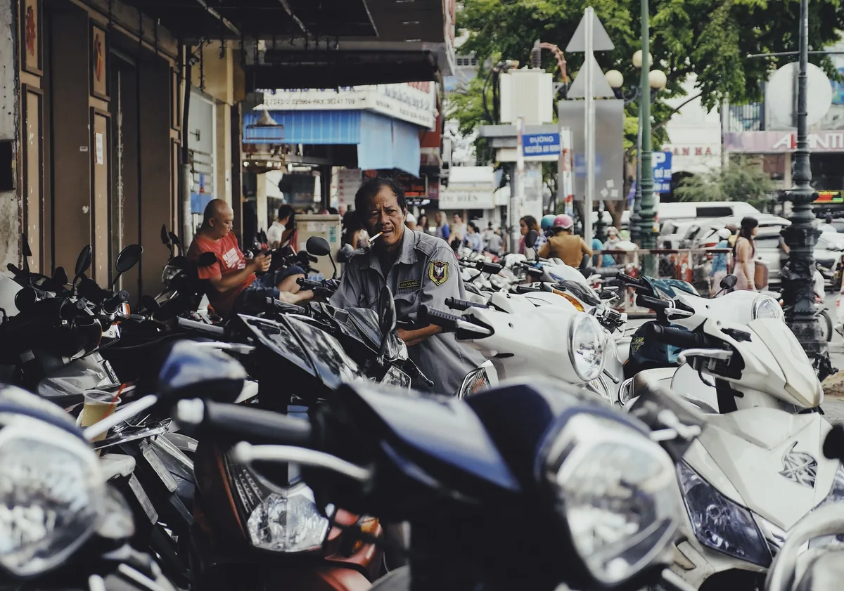 A parking attendant smokes a cigarette amid rows of parked motorbikes on a busy street in Ho Chi Minh City.