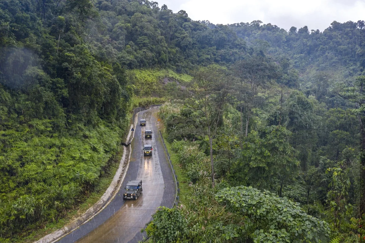 Military-style jeeps travel a winding rainy road through dense jungle along the former DMZ near Hue.