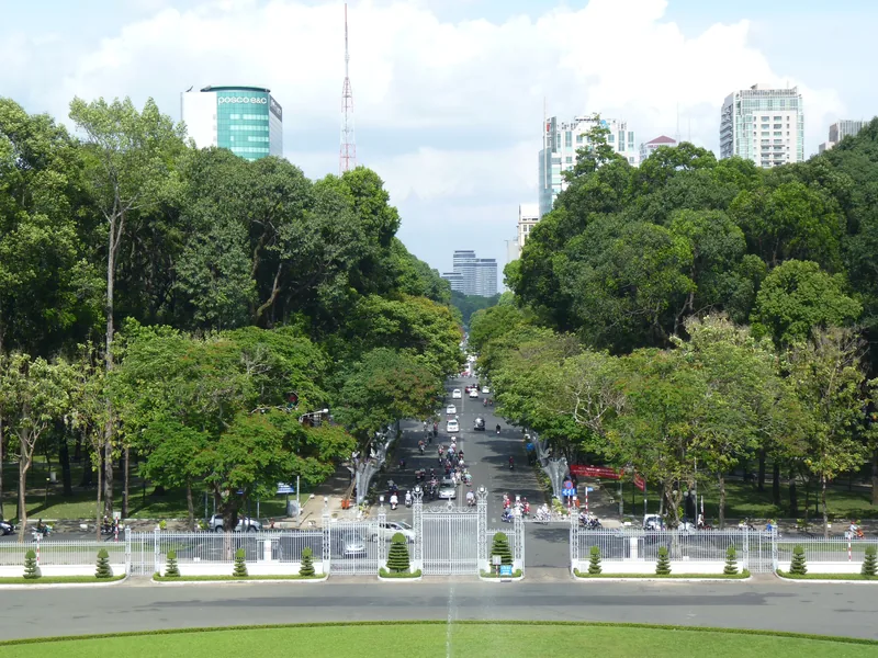 A tree-lined boulevard leads to city skyscrapers, viewed from an elevated gate in Ho Chi Minh City.