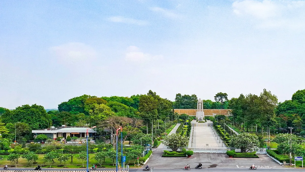 An aerial view of a memorial monument and wide pathway surrounded by lush greenery at a cemetery in Ho Chi Minh City.
