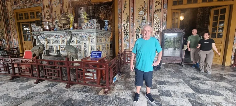 A tourist poses near an ornate ancestral altar with crane statues inside a Hue palace hall.