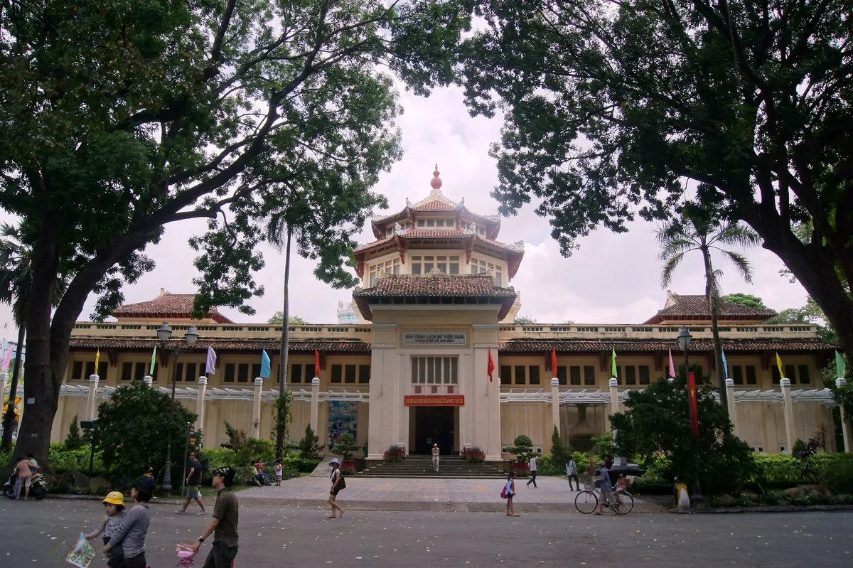 The Vietnamese-style pagoda tower and colonial facade of a history museum in Ho Chi Minh City, framed by shady trees.