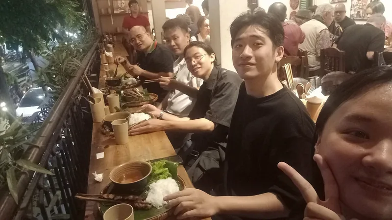 Friends enjoy grilled skewers and rice at a lively balcony restaurant in Hanoi.