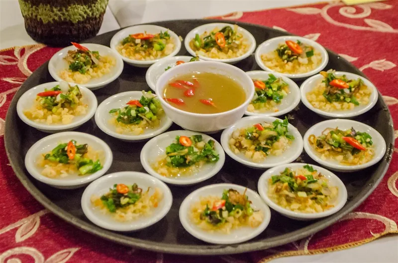 Small dishes of Hue-style banh beo topped with herbs and chili, arranged around a bowl of dipping sauce.