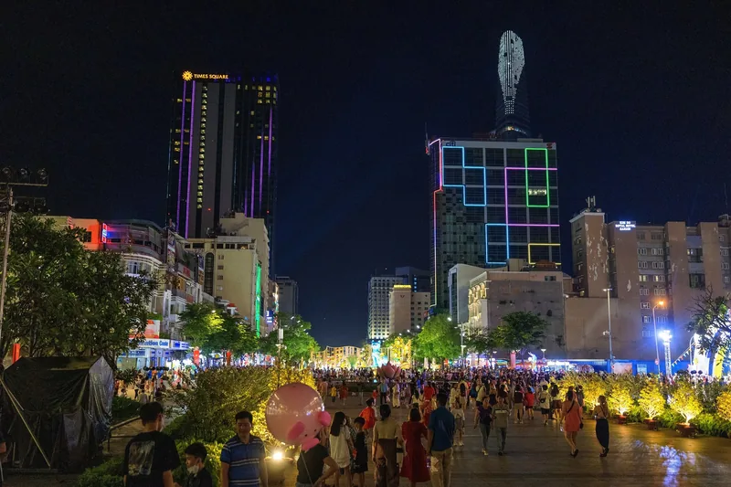 Crowds stroll along illuminated Nguyen Hue Boulevard at night, flanked by colorful skyscrapers including Times Square Ho.