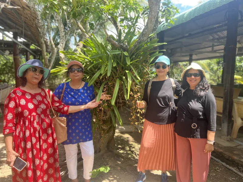 Four women in sun hats pose beside a leafy plant at a garden stop in the Mekong Delta.