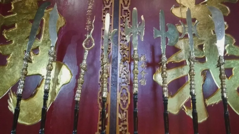 Traditional ceremonial weapons displayed against a red and gold carved wall inside a temple in Ho Chi Minh City.